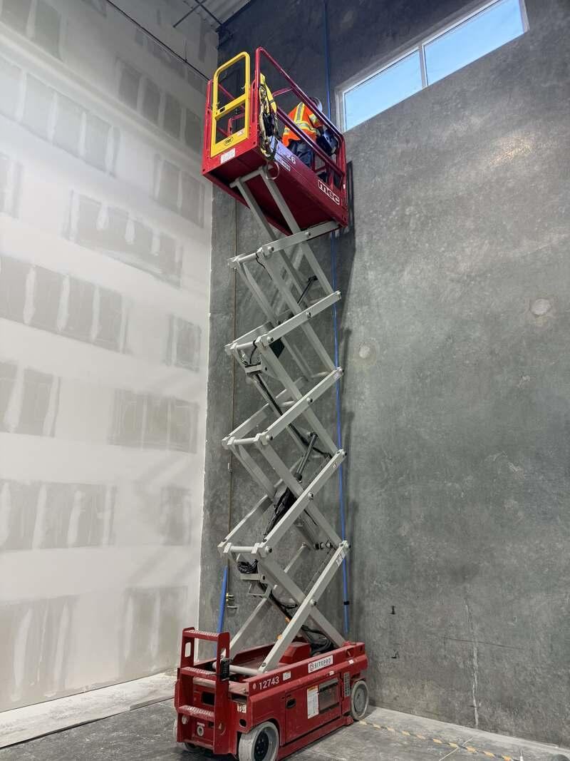 High-bay drywall work from a scissor lift in a warehouse